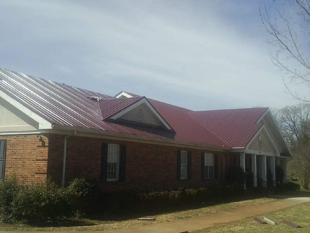 Red metal roof with gabled entries on a long brick building, from a Hail Damage Roof Repair job in Massena