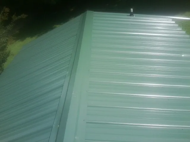 New green metal panels meeting at the ridge of a roof — Flat Roof Repair work by our crew in Massena