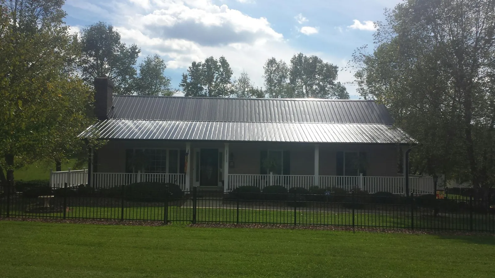 Gray metal roof on a brick ranch with a full width front porch — Gutter Guard Installation work by our crew in Massena