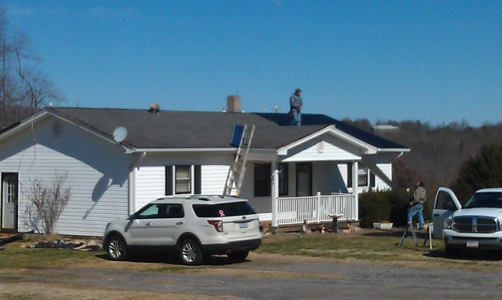 Roofers stripping shingles from a white ranch house roof in Massena