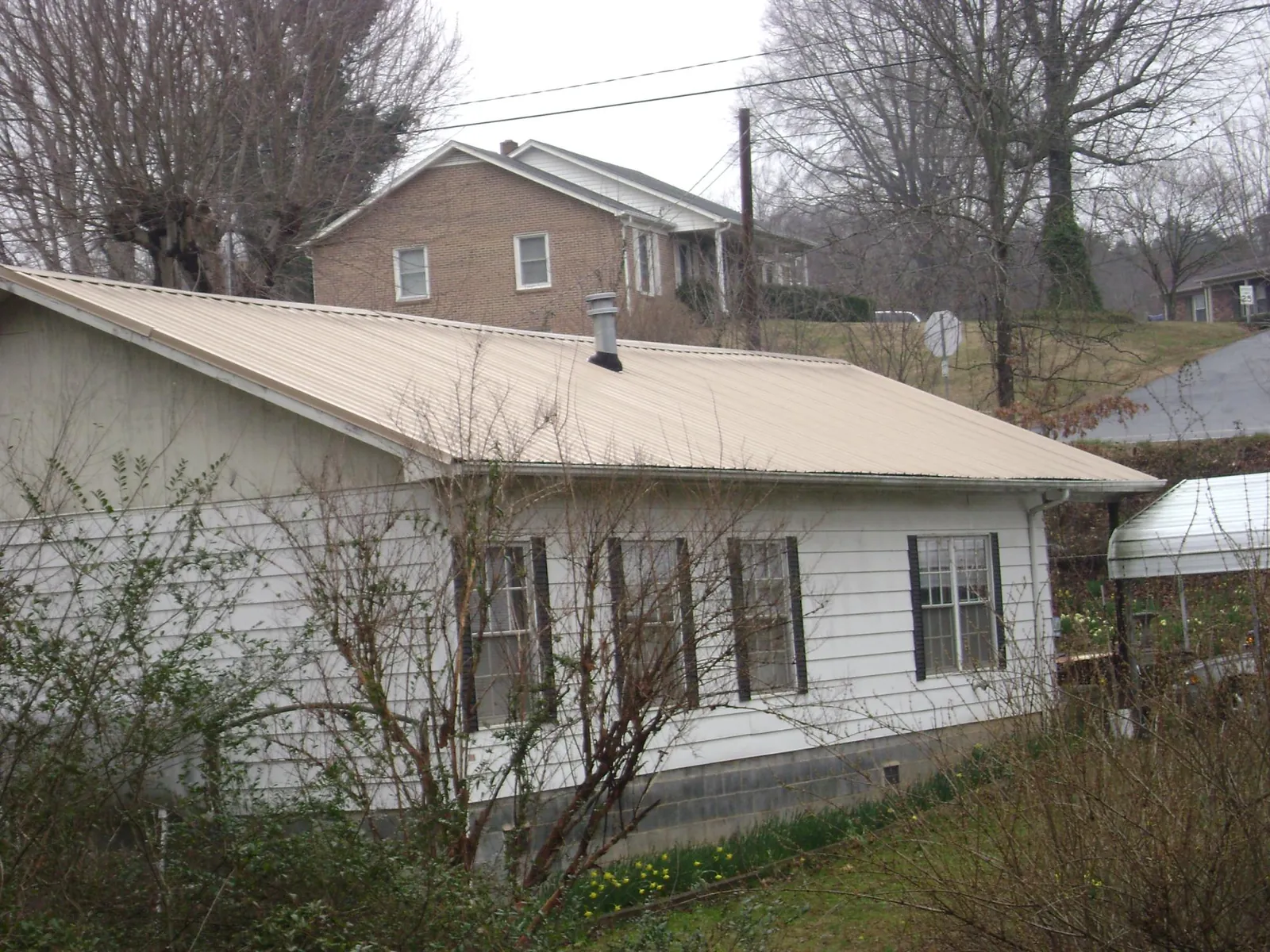 Tan metal roof on a white sided house set into a hillside — Commercial Roofing by Roofing Brothers in Massena