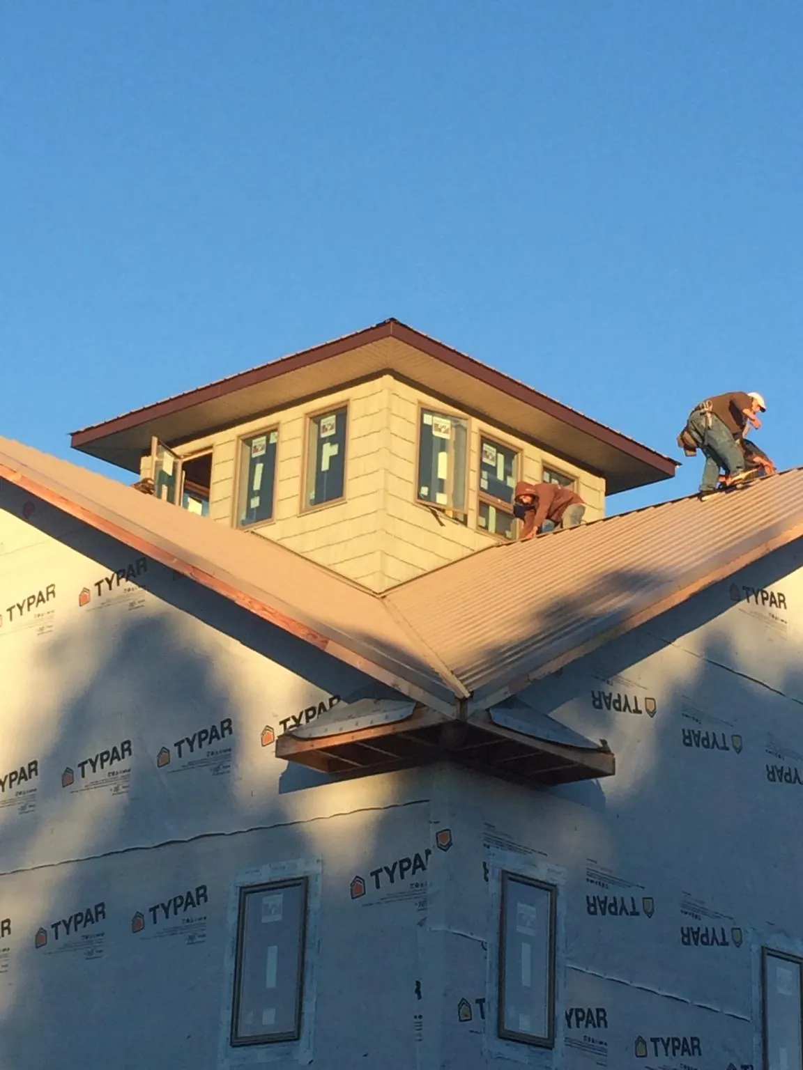 Roofers working around a rooftop cupola on a new metal roof at sunset — Roof Waterproofing in Massena by Roofing Brothers